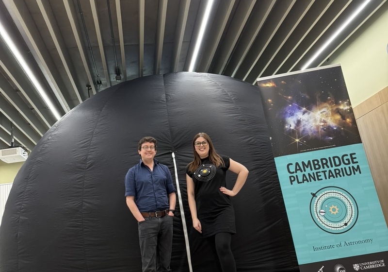 Two people standing in front of an inflatable planetarium dome 